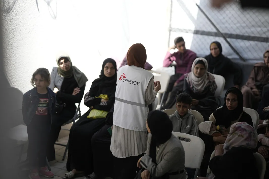 Zdravotnický pracovník Lékaři bez hranic vysvětluje pacientům fakta o podvýživě před vstupem na vyšetření. Pásmo Gazy, 2025.